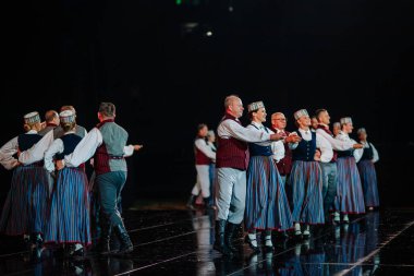 Valmiera, Letonya - 7 Haziran 2025 - GAUJA 80 'deki geleneksel Letonya halk dansları kolajı, renkli kostümlü dansçıları gece aydınlatmalı bir sahnede sergiliyorlar..
