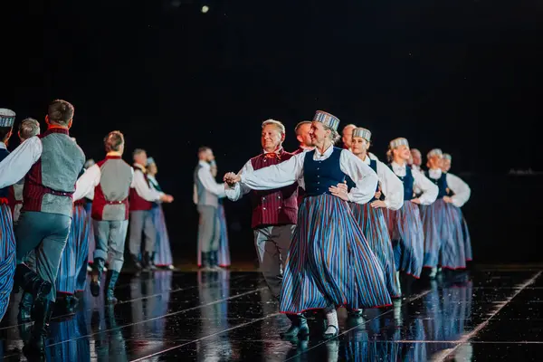 Valmiera, Letonya - 7 Haziran 2025 - GAUJA 80 'deki geleneksel Letonya halk dansları kolajı, renkli kostümlü dansçıları gece aydınlatmalı bir sahnede sergiliyorlar..