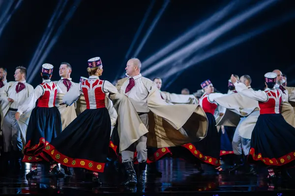 Valmiera, Letonya - 7 Haziran 2025 - GAUJA 80 'deki geleneksel Letonya halk dansları kolajı, renkli kostümlü dansçıları gece aydınlatmalı bir sahnede sergiliyorlar..