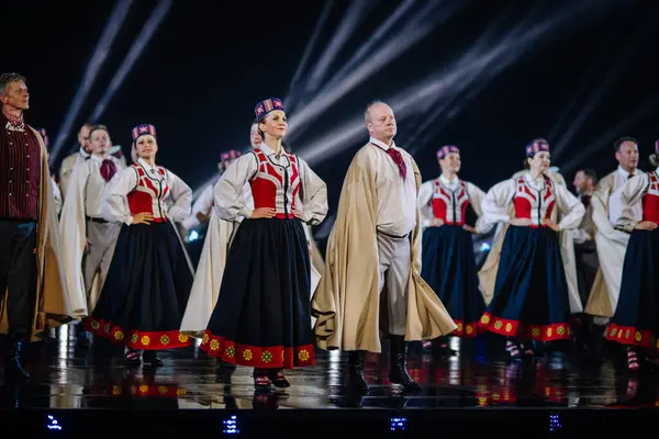 Valmiera, Letonya - 7 Haziran 2025 - GAUJA 80 'deki geleneksel Letonya halk dansları kolajı, renkli kostümlü dansçıları gece aydınlatmalı bir sahnede sergiliyorlar..