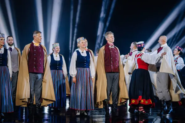 Valmiera, Letonya - 7 Haziran 2025 - GAUJA 80 'deki geleneksel Letonya halk dansları kolajı, renkli kostümlü dansçıları gece aydınlatmalı bir sahnede sergiliyorlar..