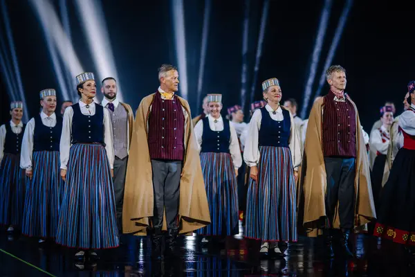 Valmiera, Letonya - 7 Haziran 2025 - GAUJA 80 'deki geleneksel Letonya halk dansları kolajı, renkli kostümlü dansçıları gece aydınlatmalı bir sahnede sergiliyorlar..