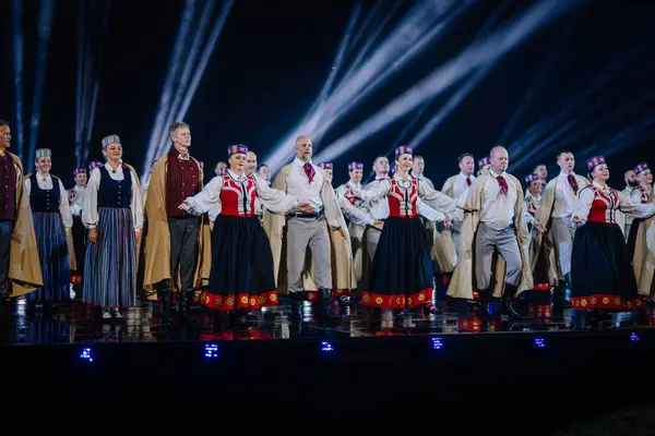 Valmiera, Letonya - 7 Haziran 2025 - GAUJA 80 'deki geleneksel Letonya halk dansları kolajı, renkli kostümlü dansçıları gece aydınlatmalı bir sahnede sergiliyorlar..