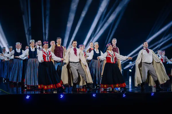Valmiera, Letonya - 7 Haziran 2025 - GAUJA 80 'deki geleneksel Letonya halk dansları kolajı, renkli kostümlü dansçıları gece aydınlatmalı bir sahnede sergiliyorlar..