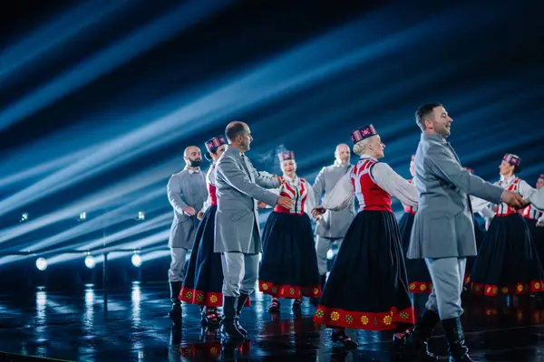 Valmiera, Letonya - 7 Haziran 2025 - GAUJA 80 'deki geleneksel Letonya halk dansları kolajı, renkli kostümlü dansçıları gece aydınlatmalı bir sahnede sergiliyorlar..