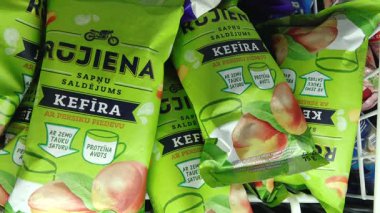 Valmiera, Letonya - 15 Haziran 2025 - Bir dondurucunun içinde şeftali aromalı ambalajlı Rjiena kefir dondurması, canlı yeşil ambalajlar ve meyve çizimleri sergileniyor.