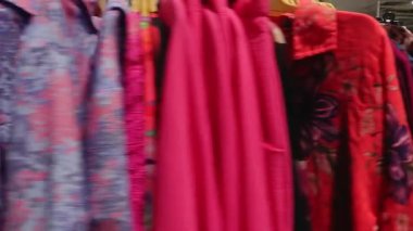 Valmiera, Letonya - 15 Haziran 2025 - Bir butikte elbise askısı, renkli, desenli elbiseler hareket halinde bulanık, mavi, pembe ve çiçekli kumaşlar.