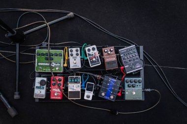 Liepa, Letonya - 27 Haziran 2025 - Çeşitli gitar ve bas efekt pedalları ve kablolar içeren bir pedal düzeneği, yukarıdan karanlık bir sahne zemininde fotoğraflandı.