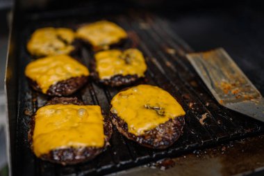 Eritilmiş çedar peyniri ile sulu sığır burger köfteleri sıcak ızgarada cızırdıyor, yağlı ve yanında metal bir spatula var..