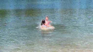 Güneşli bir günde, sakin bir gölde neşeyle sıçrayıp oynayan iki kız, suda kaygısız bir yaz anının tadını çıkarıyorlar..