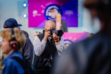 Cesis, Letonya - 20 Haziran 2025 - Kel bir erkek fotoğrafçı, DSLR kamerasıyla, canlı bir atmosferde parlayan kulaklık takan insanlarla dolu sessiz bir disko etkinliğinde anlar yakalıyor..