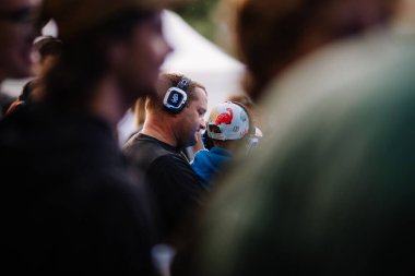 Cesis, Letonya - 20 Haziran 2025 - Kulaklık takan bir adam ve genç bir çocuk sessiz bir disko etkinliğinin tadını çıkarıyorlar. Sahne bulanık bir kalabalık tarafından çerçeveleniyor, neşeli atmosferde samimi bir an yaratıyor..