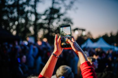 Cesis, Letonya - 20 Haziran 2025 - Bir kişi, alacakaranlıkta sessiz bir disko kalabalığını kaydetmek için bir akıllı telefonu soydu. Telefon ekranında açık hava etkinliklerinde insanların kulaklıkla dans ettiği görülüyor..