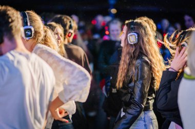 Cesis, Letonya - 20 Haziran 2025 - İnsanlar gece sessiz bir diskodan hoşlanıyorlar, renkli ışıklar ve canlı bir kalabalık ile çevrili LED kulaklıklar takıp dans ediyorlar ve gülümsüyorlar..