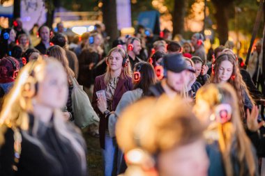 Cesis, Letonya - 20 Haziran 2025 - Renkli LED kulaklık takan bir kalabalık, açık hava parkı ortamında, müzik ve dansa dalmış, sessiz bir diskonun keyfini çıkarıyor..