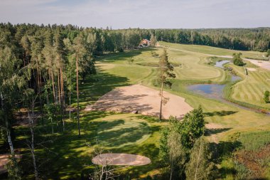 Sigulda, Letonya - 16 Haziran 2025 - Güneşli bir günde yeşillikler, sığınaklar, göletler, çayırlar ve ormanların bulunduğu bir golf sahasının manzaralı manzarası.