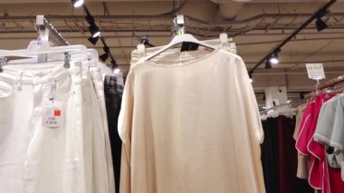 Valmiera, Letonya - 8 Temmuz 2025 Bej saten bluz ve diğer kıyafetlerle çevrili bir giyim mağazasında aynı etek sergileniyor. Moda mağazasının bir parçası..