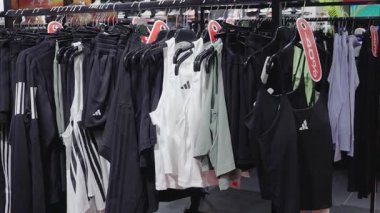 Valmiera, Letonya - 8 Temmuz 2025 - Bir perakende mağazasında askılara astıkları kolsuz bluzlar, taytlar ve şortlar dahil olmak üzere çeşitli Adidas spor giyim ürünleri, görünür satış tabelaları ve Adidas markası.