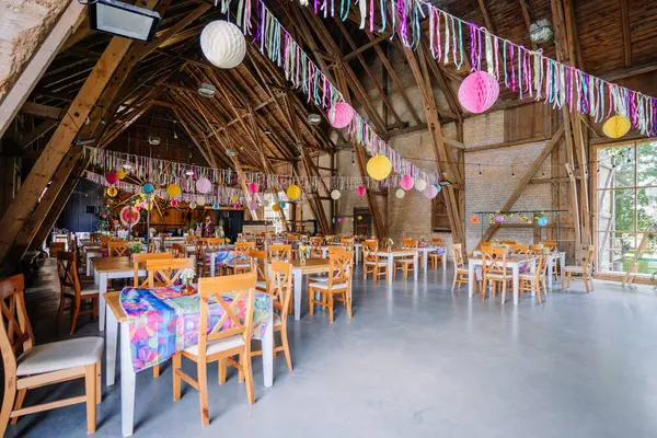 Sigulda, Letonya - 18 Temmuz 2025 - Renkli flamalar, kağıt fenerler ve festival için hazırlanan masalarla süslenmiş köy ahırı iç mimarisi. Kopya alanı ile parlak ve neşeli bir atmosfer.