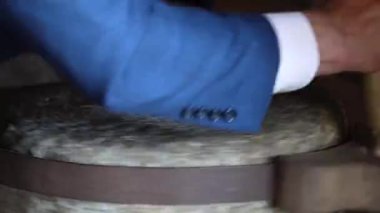 Mavi takım elbiseli bir adamın, tahılı un haline getirmek için geleneksel bir değirmeni elle döndürüp dönen tekerleğin hareket bulanıklığını gösteren yakın plan fotoğrafı..