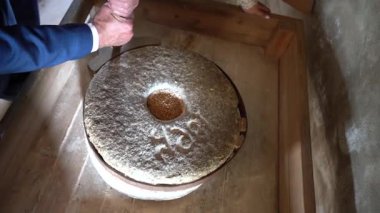 İnsan, tahıllarla dolu geleneksel bir taş değirmenini kullanarak un öğütüyor. Bu da tarihi gıda üretim sürecini gösteriyor..