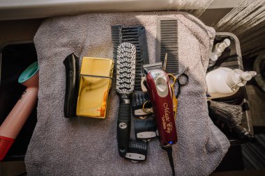 Cesis, Letonya - 17 Temmuz 2025 - Kırpıcı, tarak, makas, saç fırçası, budama makinesi ve kuaför salonundaki şekillendirme ürünleri de dahil olmak üzere gri bir havlunun üzerindeki profesyonel berber aletleri.