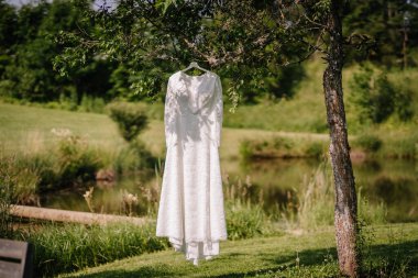 Beyaz dantelli bir gelinlik, sakin yeşil bir çayırda asılı duran bir ağaçtan sarkan, sakin ve kırsal bir gelin anını yakalıyor..