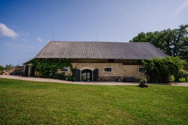 Cesis, Letonya - 17 Temmuz 2025 - Yeşillik ve açık mavi gökyüzü ile çevrili büyük ahşap çatılı büyüleyici bir taştan ahır, kırsal alanlar ve düğünler için mükemmel.