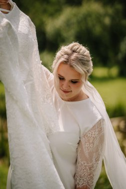 Dantel desenli bornozlu gelin, doğal ışıkta gelinliğine hayran, açık hava ortamındaki büyük güne hazırlanıyor..
