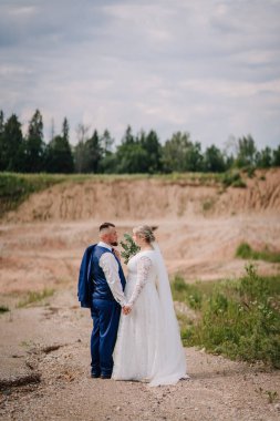 Bir gelin ve damat, manzaralı, kırsal bir arazide kayalık bir yolda dururken el ele tutuşuyorlar. Damat ceketini tutuyor ve birbirlerine sevgiyle bakıyorlar..