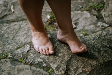 Cesis, Letonya - 17 Temmuz 2025 - Yaşlanmış taş kaldırımların üzerinde duran cilalı tırnaklı çıplak ayaklı yakın plan, muhtemelen Svetavots 'ta, dünyayla doğal teması gösteriyor..