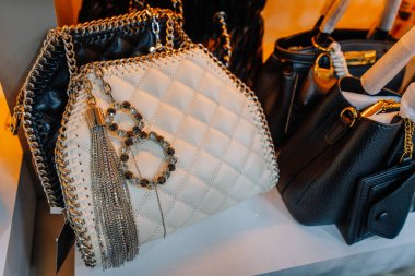 Kemer, Turkey - September 19, 2025 - Close-up of luxury-style handbags with chain straps, including a white quilted bag adorned with rhinestone keychains and metallic tassel, on a store shelf.