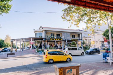 Kemer, Turkey - September 19, 2025 - Street view of a commercial shopping area with clothing stores, signs, cars, and a yellow taxi in front of the Otantik and Molly Bessa storefronts