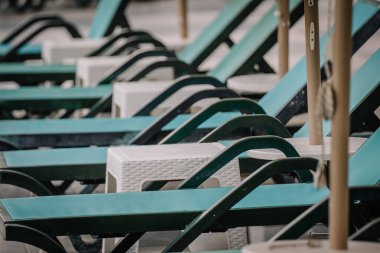 Boş turkuaz şezlonglar ve beyaz yan masalar. Havuz kenarında. Düzenli ve güneş şemsiyesi altındaki misafirler için hazır..