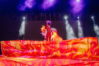 Kemer, Turkey - September 21, 2025 - A Raza Urbana performer stands powerfully on stage above flaming red fabric, framed by fire visuals and dramatic lighting during a dynamic dance performance.