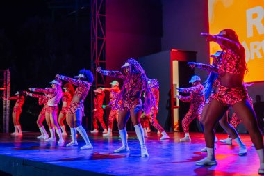 Kemer, Turkey - September 21, 2025 - Dancers in vibrant red patterned outfits perform a powerful urban dance routine on stage during the Raza Urbana event under bright, colorful lights.
