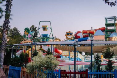 Kemer, Turkey - September 21, 2025 - Colorful outdoor water park with slides, splash zones, and playful decorations like a smiling sun and giant pineapple, captured during twilight.