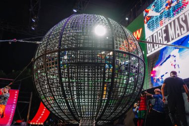 Kemer, Turkey, September 22, 2025 - Large steel globe cage in center stage with performers inside during a stunt at the Extreme Globe Show, surrounded by crew and spectators under stage lights.