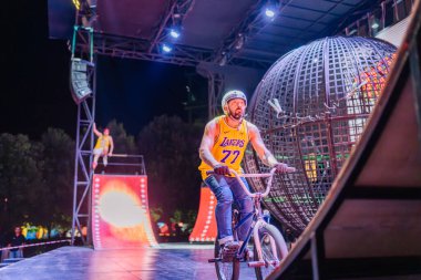 Kemer, Turkey, September 22, 2025 - BMX rider in a yellow jersey rides near the steel globe while another performer prepares on the ramp during the Extreme Globe Show under bright stage lights.