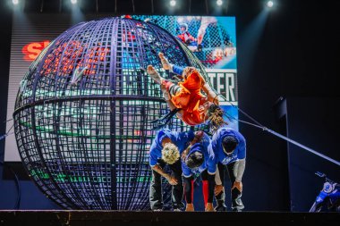 Kemer, Turkey, September 22, 2025 - Performer executes a mid-air flip over teammates during the Extreme Globe Show, with a steel globe cage and stage lights creating a thrilling backdrop.