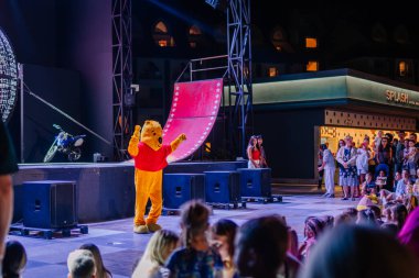 Kemer, Turkey, September 22, 2025 - A performer in a bear costume entertains families and children during the Extreme Globe Show at night, near the stunt stage and motorcycle setup.