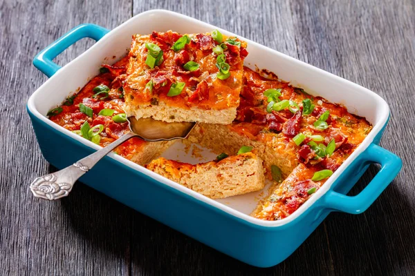 Riced Cauliflower Breakfast Bake topped with melted cheese, green onion and crispy fried bacon in baking dish on dark wooden table