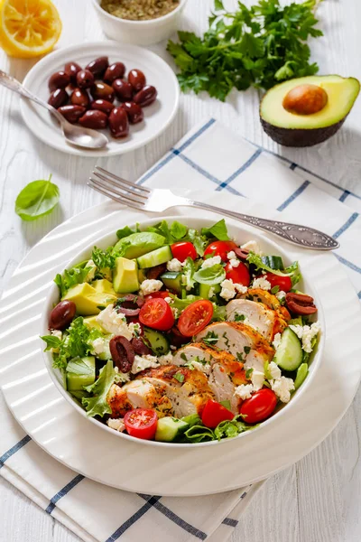 stock image Mediterranean Rotisserie Chicken Salad with avocado, lettuce, kalamata olives, cucumber, tomato and crumbled feta cheese in white bowl on white wood table, vertical view, close-up