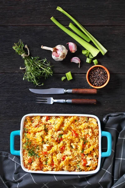 Chicken Pot Pie Fusilli pasta Bake with celery, corn, green peas, carrots , topped with panko breadcrumbs in baking dish on dark wood table, vertical view from above