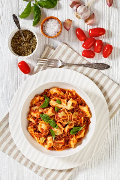 tortellini in ground beef tomato sauce in white bowl on white wood table,  vertical view from above