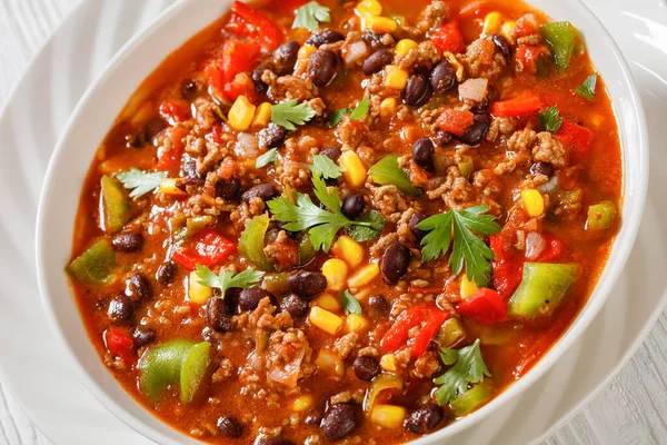 close-up of taco soup of ground beef, tomatoes, chopped green chilis, onions, corn, red beans and taco seasoning in white bowl, american cuisine