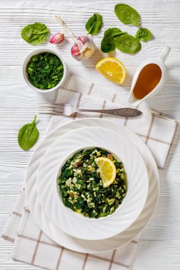 Spanakorizo, Greek spinach and rice pilaf with lemon, dill, scalion in white bowl on white textured wooden table, vertical view from above clipart