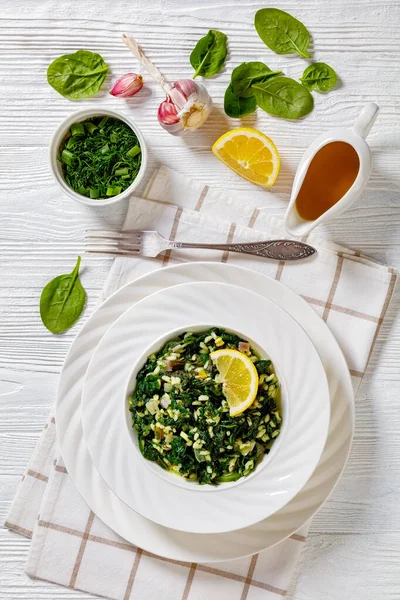 stock image Spanakorizo, Greek spinach and rice pilaf with lemon, dill, scalion in white bowl on white textured wooden table, vertical view from above