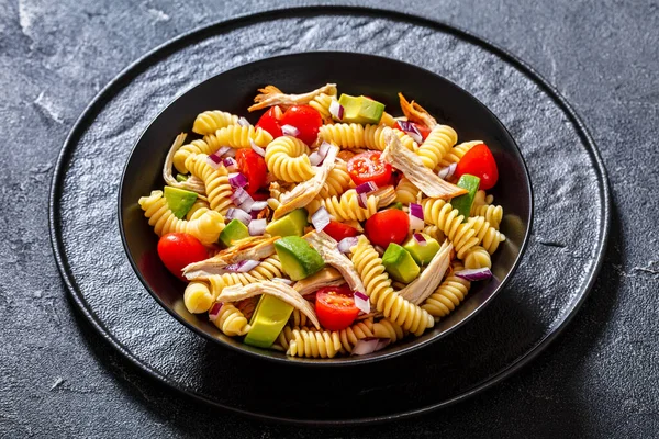 Healthy Chicken Pasta Salad with Avocado, Tomato, and olive oil and vinegar dressing in black bowl on table