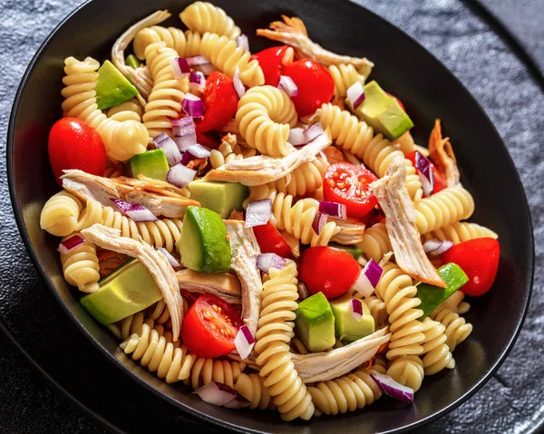 close-up of Healthy Chicken Pasta Salad with Avocado, Tomato, and olive oil and vinegar dressing in black bowl